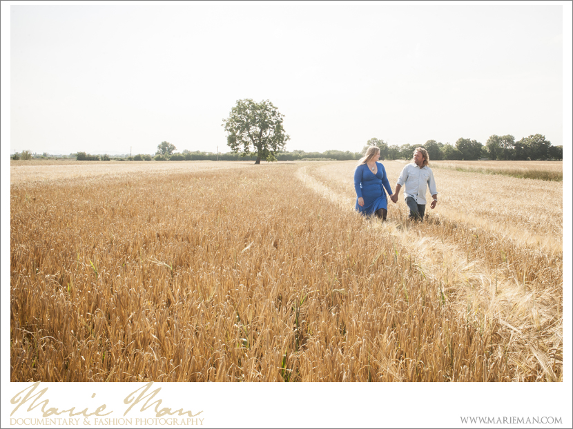 Emily & Paul walking through a golden field of grass - Cotswold Engagement Photography